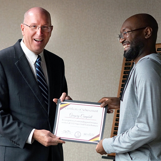 Dean of the Dillard College of Business Administration poses with a student, as they both laugh and smile, celebrating the student's achievements.