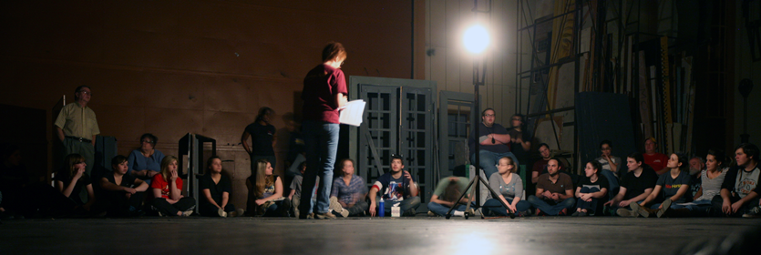 Student on stage reading among his peers, who are listening to him perform.