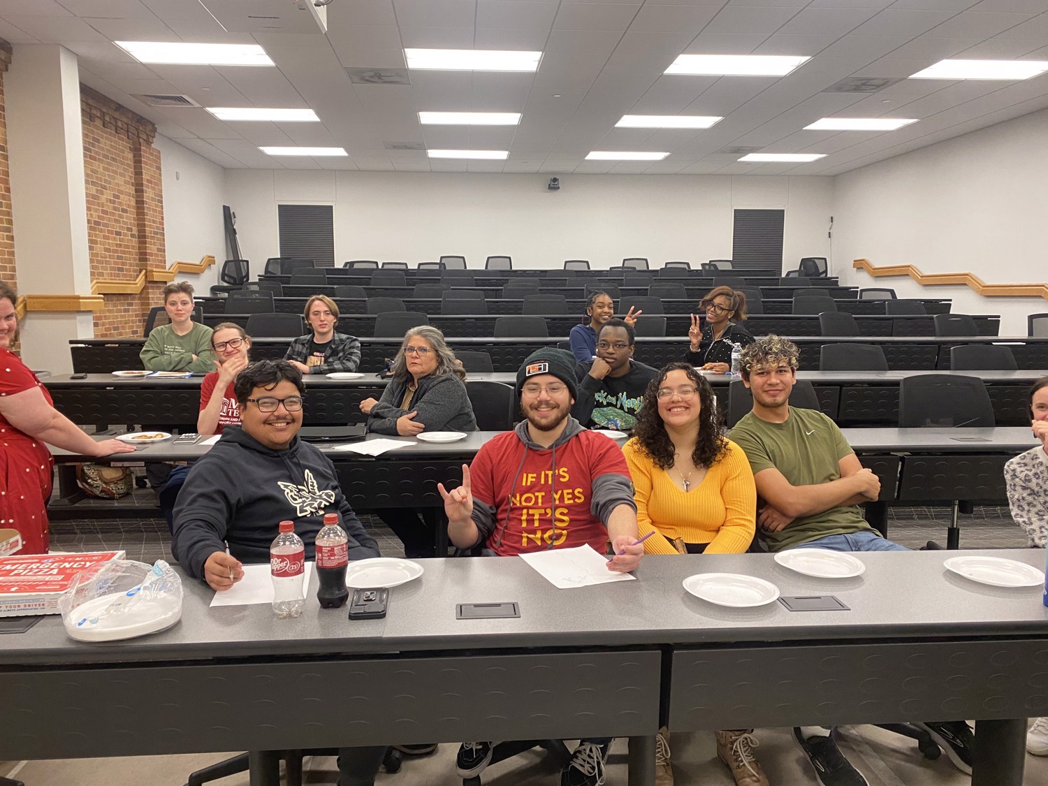 A group of students smiling and eating pizza in a classroom