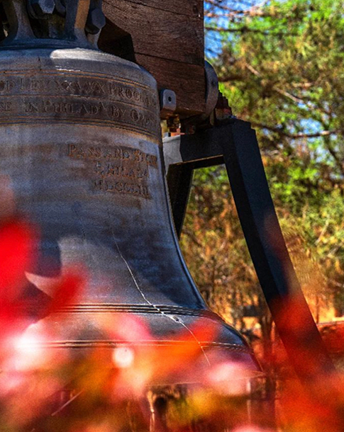 Blazing orange fall leaves blanket the Hardin Administration Building lawn, surrounding the replica of the Liberty Bell.