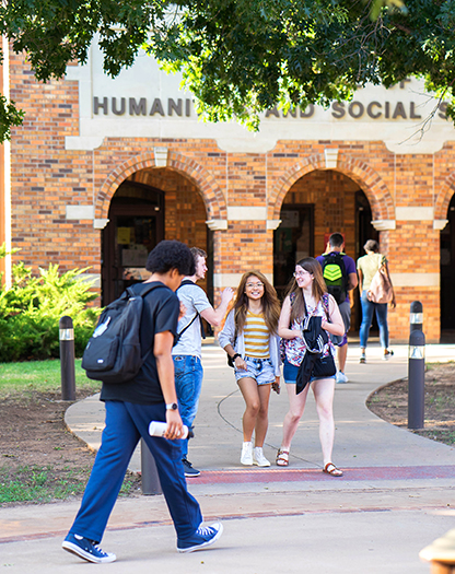 Several students walking enter and exit Prothro-Yeager College of Humanities & Social Sciences on a bright, sunny day.