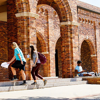 Two students enter in to Moffett Library as third student rests against the archway outside the entrance.
