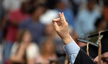 A graduating student holds up the Mustangs Hand Sign during the commencement ceremony.