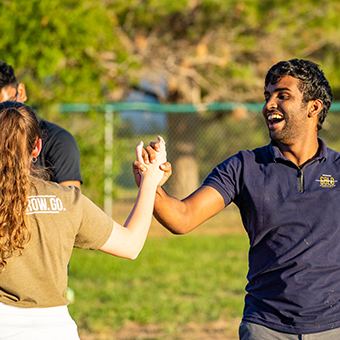 Two students laugh and shake hands during an event.