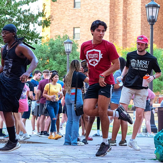 A group of students gather and dance in the Legacy Courtyard during an event.