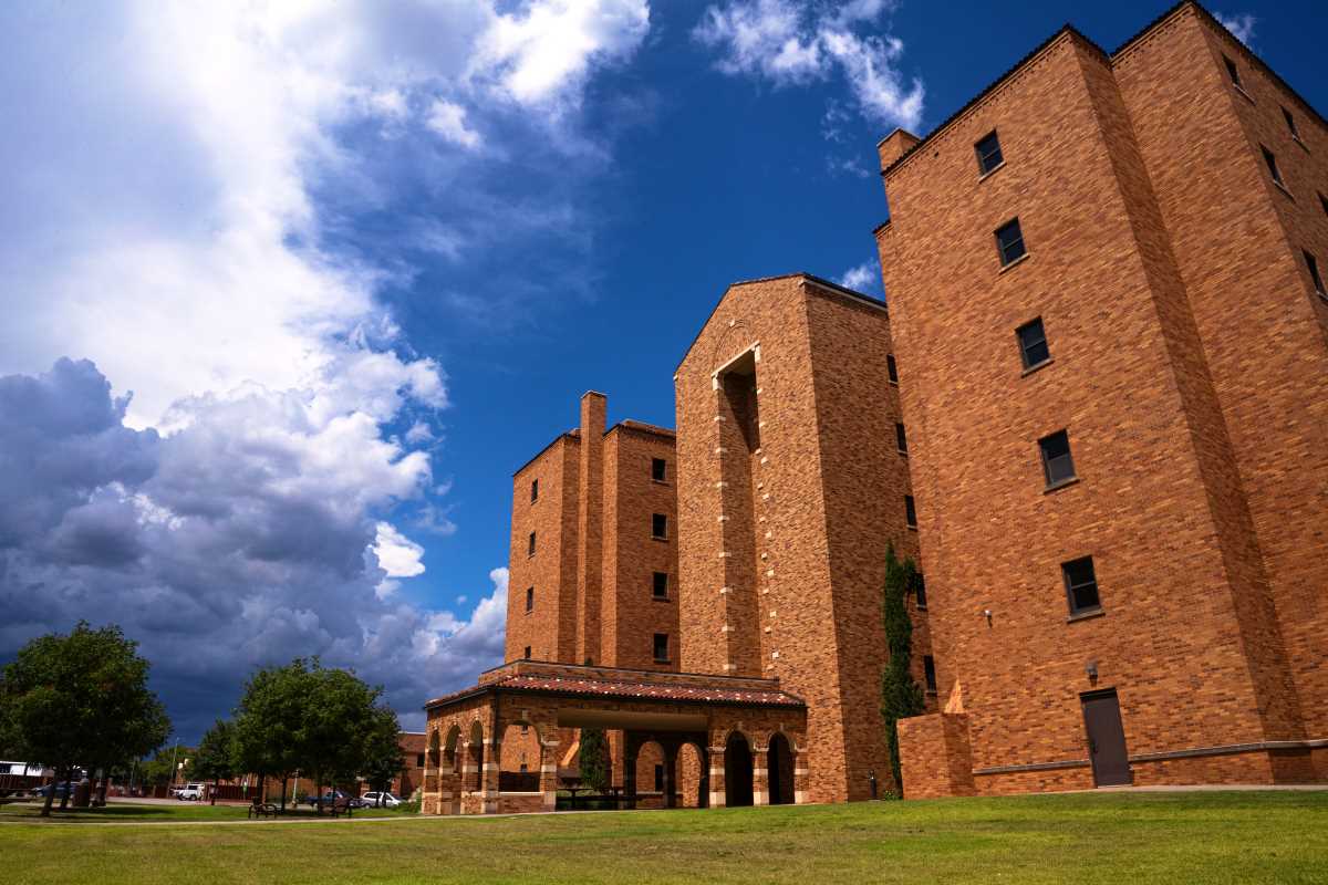 Killingsworth Hall's west entrance exterior on a late spring day. All six of Killingsworth's floors can be seen along with the covered entryway and the grass courtyard surrounding it. picnic benches can be seen under the covered entryway as rain clouds roll in from the left starting to take over the blue sky.