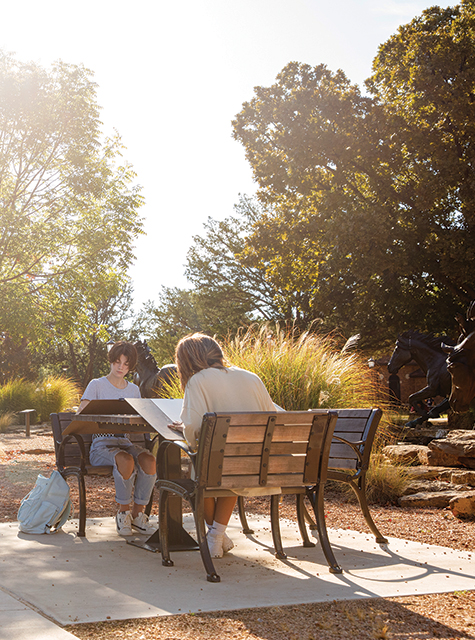 Students working together while sitting outside near the Spirit of the Mustangs statue.