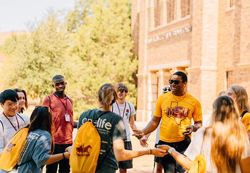 A group of students are gathered, engaged in conversation, outside of the Dillard College of Business Administration.