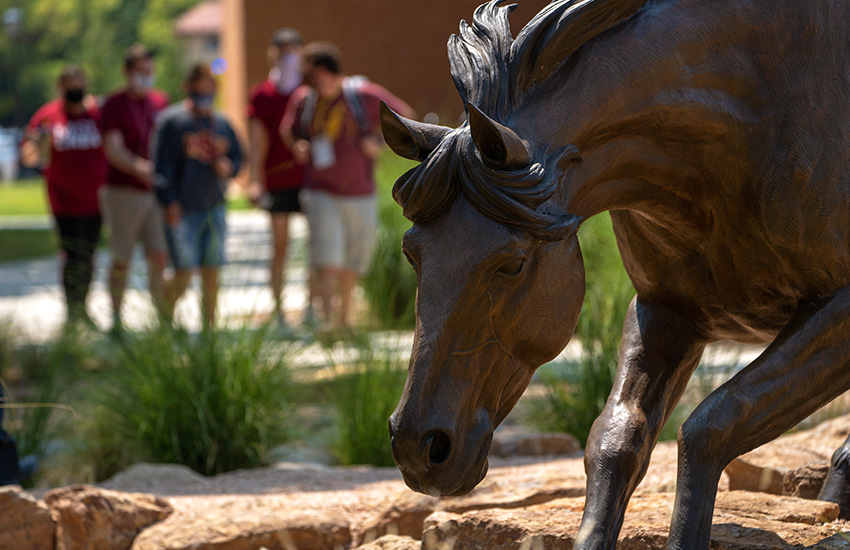 Close up image of one of the mustangs at the Spirit of the Mustangs statue with students walking in the background.