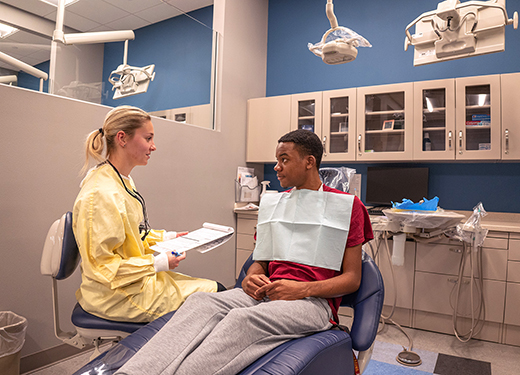 Dental hygiene students talking inside one of their labs that is set up like a dentist's office.